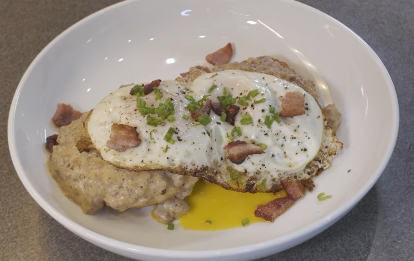 Buttermilk biscuits under sausage gravy topped with a fried egg and bacon