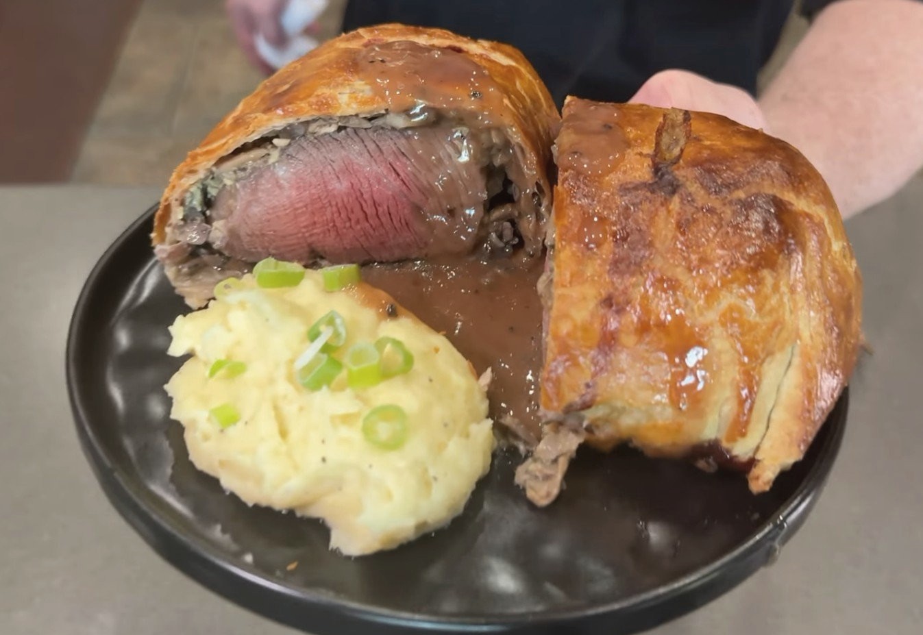 Mini beef Wellington sliced open showing a medium rare center, served with mashed potatoes and pan sauce