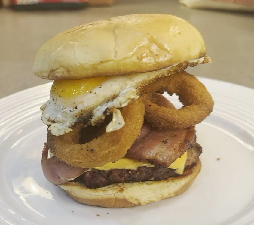 Towering bacon egg and cheese burger stacked with onion rings and a fried egg