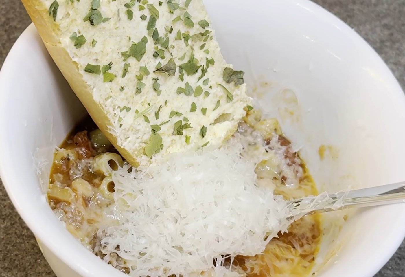 Bowl of pasta fazool topped with fresh grated parmesan and a slice of garlic bread
