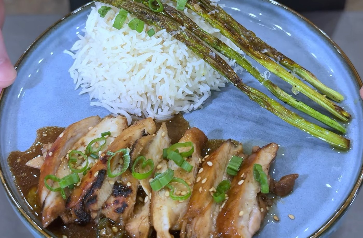Szechuan peppercorn chicken with rice and roasted asparagus, garnished with scallions and sesame