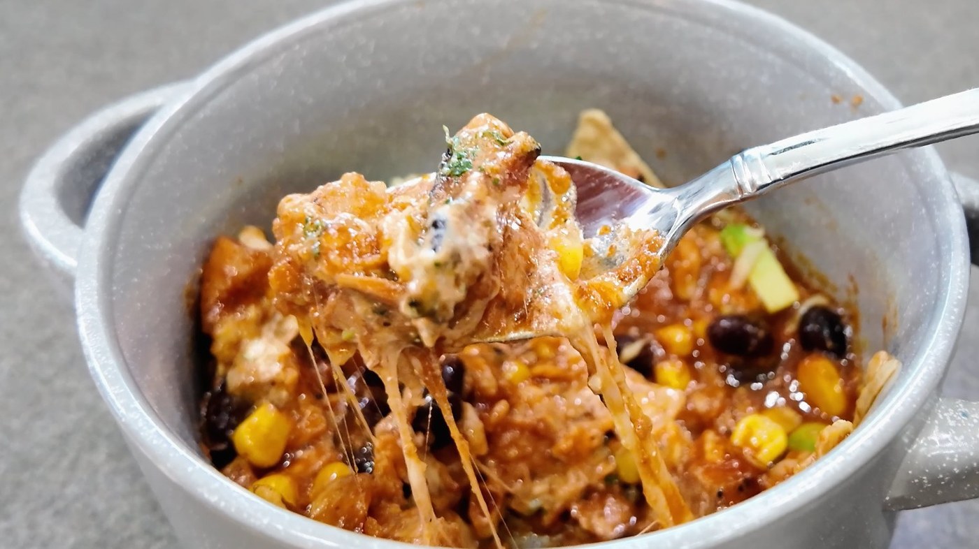 A spoonful of chicken tortilla soup lifted from the bowl with melted Monterey Jack pulling behind it