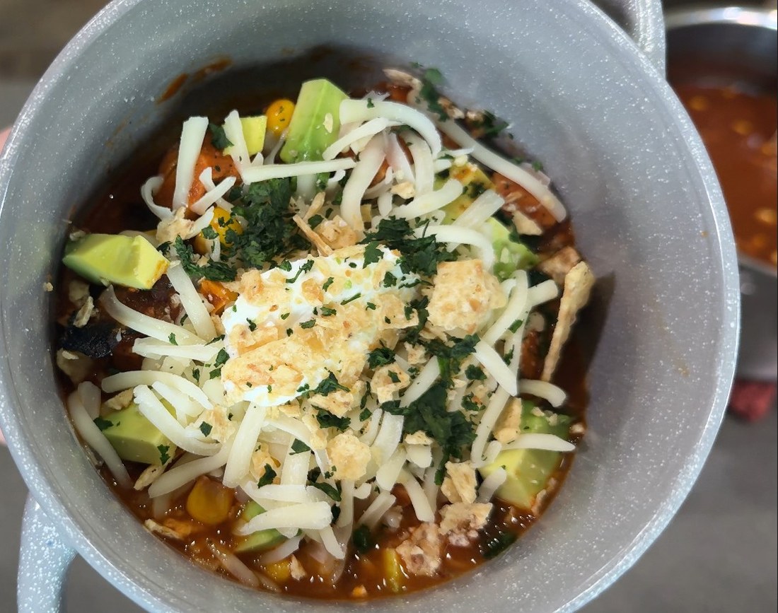 Bowl of chicken tortilla soup loaded with shredded Monterey Jack, diced avocado, sour cream, cilantro, and crumbled tortilla chips